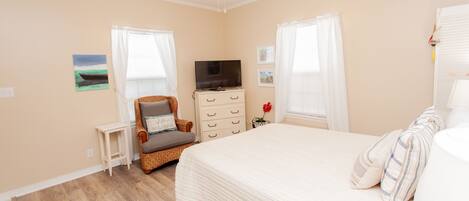 A bedroom with a bed, a television, a chair, a dresser, and a ceiling fan.