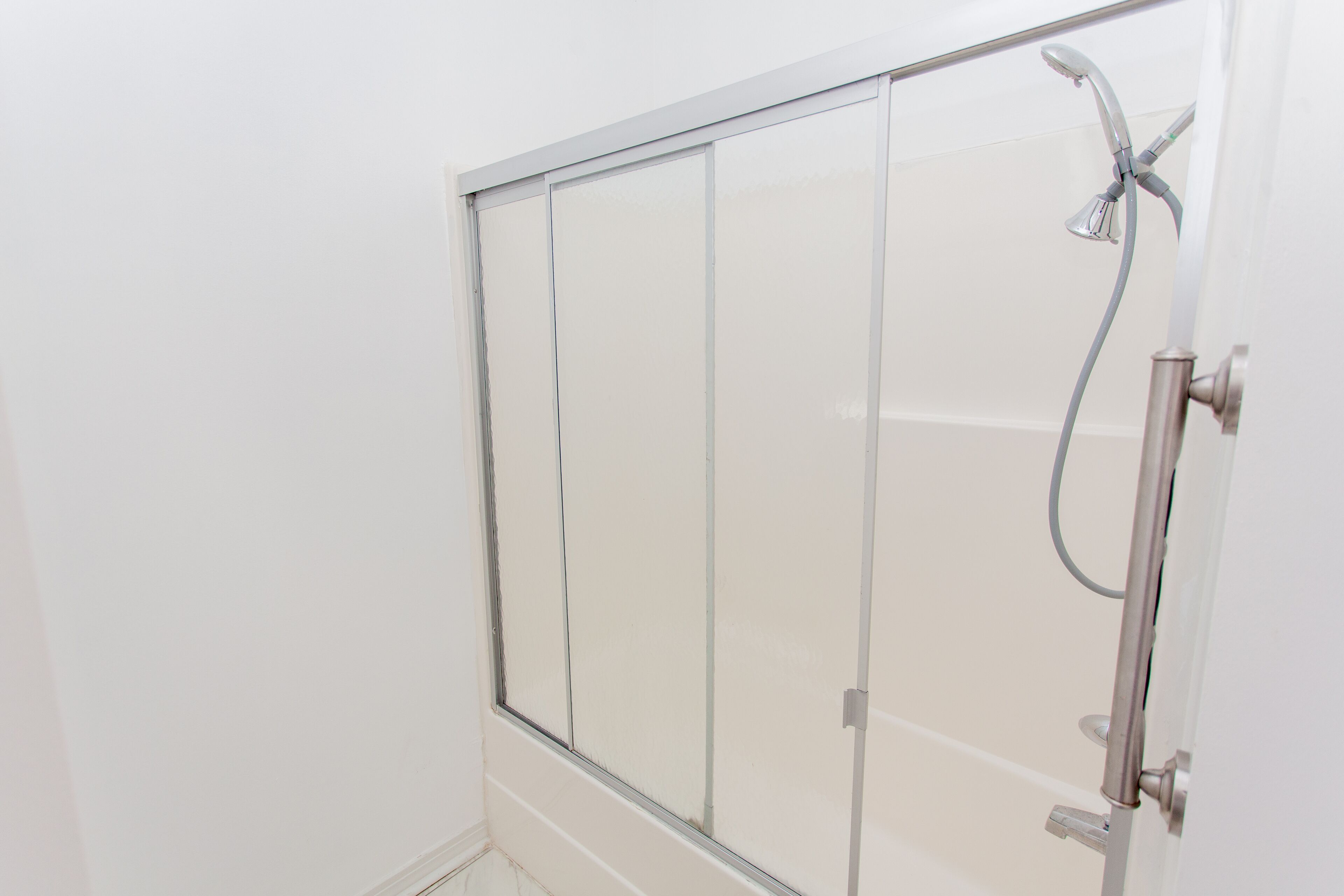 A shower enclosure with a glass door and a handheld showerhead.