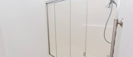 A shower enclosure with a glass door and a handheld showerhead.