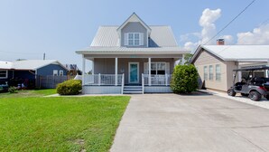 A two-story house with a front porch, a small front yard, and a golf cart parked in the driveway. - Beautiful Quaint Home Half a Block from the Beach! W/Gulf Views! (Panama City Beach)