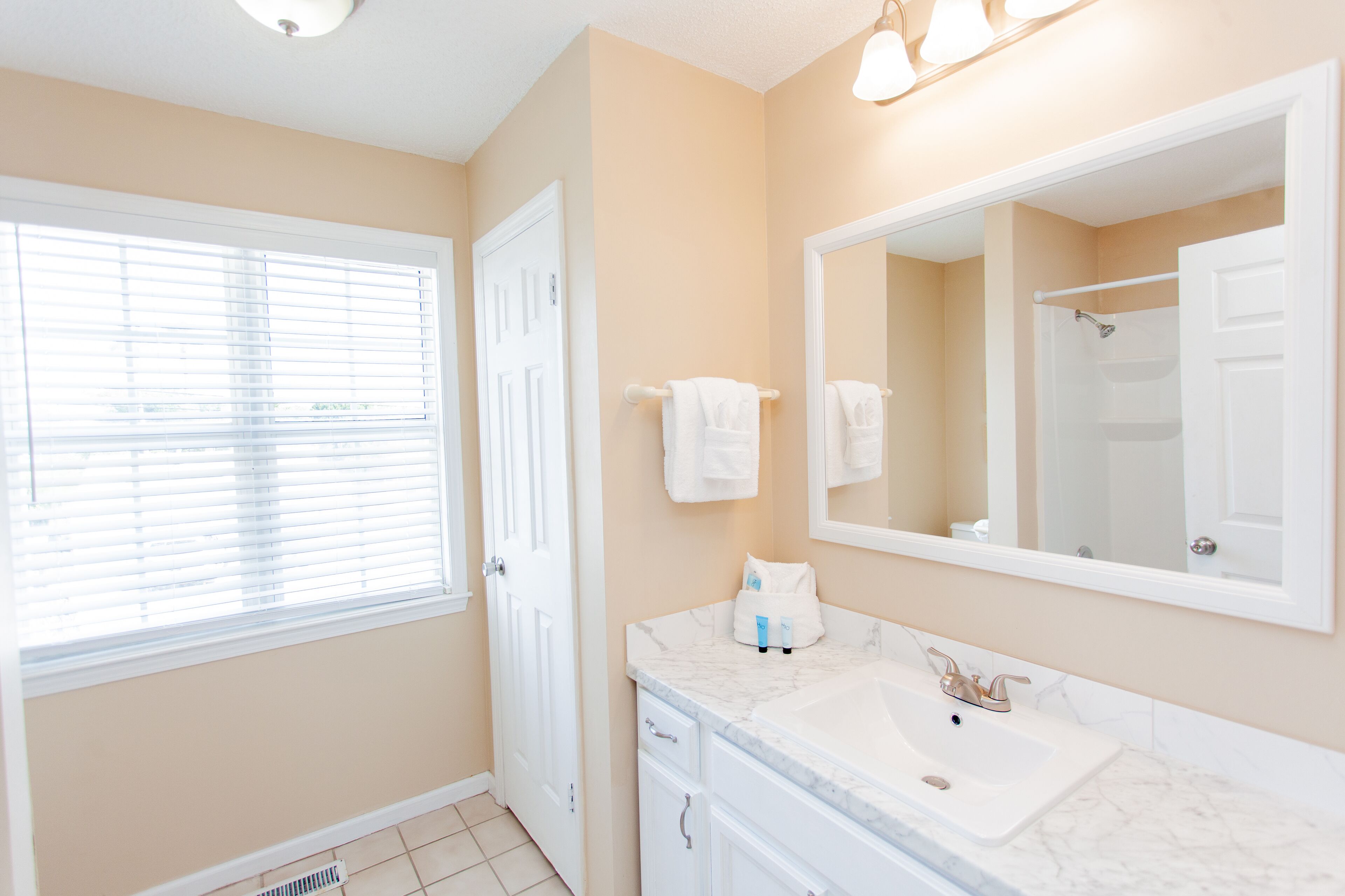 A bathroom with a white sink, a large mirror, and a window with blinds.