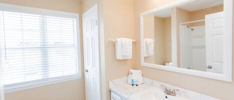 A bathroom with a white sink, a large mirror, and a window with blinds.