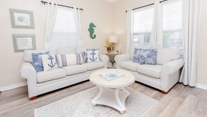 A living room with two light-colored sofas, a round coffee table, and a decorative wall piece. - Beautiful Quaint Home Half a Block from the Beach! W/Gulf Views! (Panama City Beach)