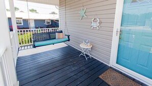 A porch with a swing, a small table, and a door with a glass panel. - Beautiful Quaint Home Half a Block from the Beach! W/Gulf Views! (Panama City Beach)