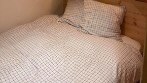 Un dormitorio con techo de madera, un espejo redondo, una mesita de noche con lámpara y una cama con colcha a cuadros.