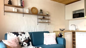 Una sala de estar con un sofá azul, una mesa de centro y una zona de cocina con microondas y lavavajillas.