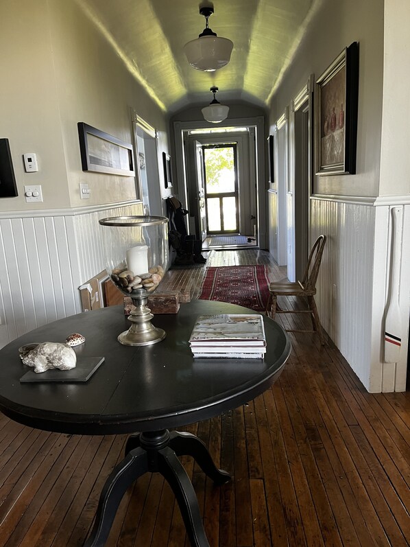Un couloir doté d’un plancher en bois, une table ronde ornée de livres et d’un objet décoratif, et une porte donnant sur une autre pièce.