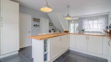 Une cuisine avec des armoires blanches, un plan de travail en bois et deux luminaires suspendus.