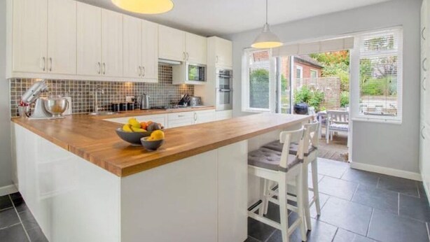 A modern kitchen with white cabinets, a wooden island, and a view of the garden through the sliding glass door.