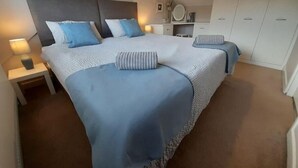 A bedroom with a large bed, two bedside tables, a nightstand, a dresser, and a mirror.