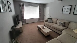 A modern living room with a beige sofa, a coffee table, and a TV on a stand.