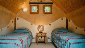A cozy attic bedroom with two beds, a small table, and a unique ceiling design. - Cabane "les 3 Complices" (Labastide de Virac)