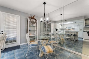 A modern kitchen with white cabinets, a glass dining table, and a mirrored backsplash.