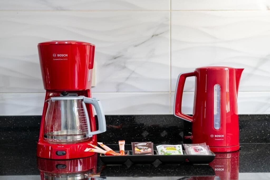 A red Bosch coffee maker and kettle on a kitchen counter with a marble backsplash.