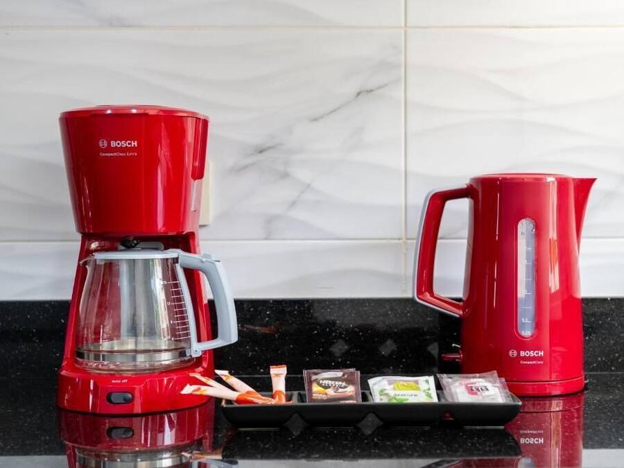 A red Bosch coffee maker and kettle on a kitchen counter with a marble backsplash.