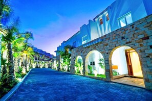 A hotel corridor with stone arches, palm trees, and a paved walkway. - DAR MRAHA APPART HOTEL (Al Bahraoyine)