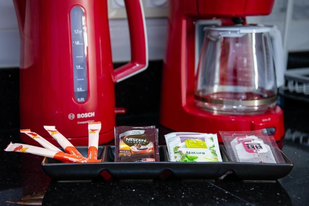 Eine Küche mit einer roten Bosch-Kaffeemaschine und einer Kaffeekanne. Auf der Arbeitsfläche liegen vier Kaffeekapseln und eine Packung Nescafé Classic.