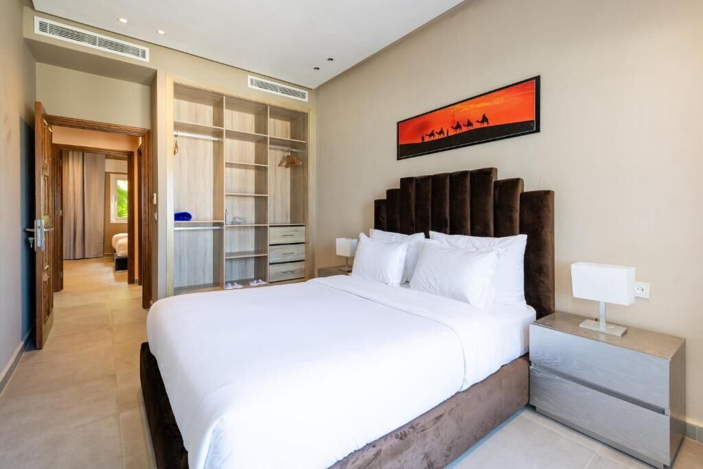 A modern hotel room with a large bed, a walk-in closet, and a painting of a sunset.