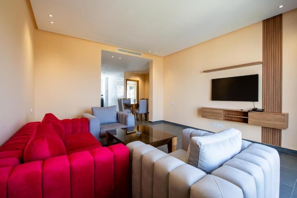 A modern living room with a red sofa, a grey sofa, a coffee table, and a flat-screen TV mounted on the wall.