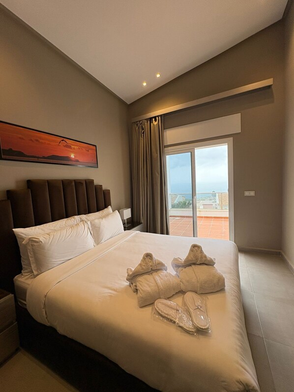 A hotel room with a large bed, a view of the city through a sliding door, and a sunset painting on the wall. - DAR MRAHA APPART HOTEL (Al Bahraoyine)