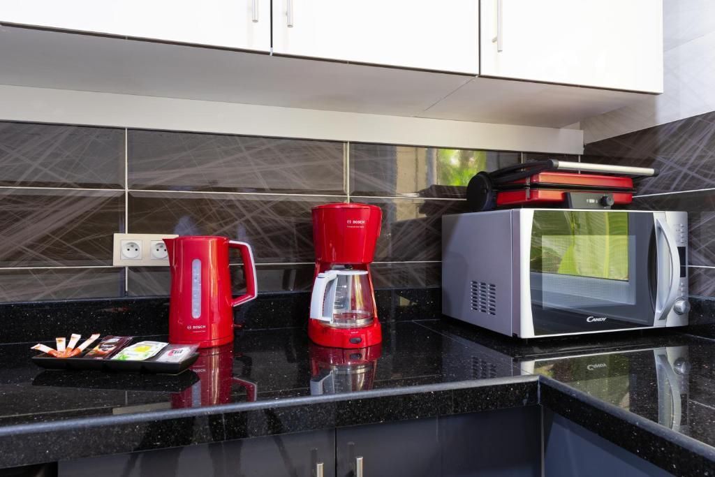 Una cocina con encimera negra, una cafetera roja, un microondas plateado y un hervidor rojo Bosch.