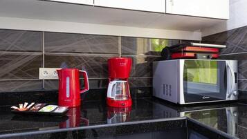 Una cocina con encimera negra, una cafetera roja, un microondas plateado y un hervidor rojo Bosch.