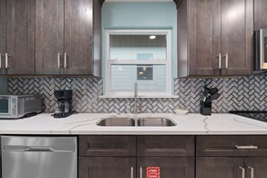 Una cocina con armarios de madera oscura, lavavajillas de acero inoxidable, cafetera y microondas.
