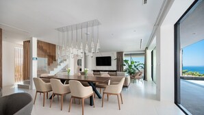 Un comedor moderno con una mesa grande y sillas, una escalera, y vista al mar.