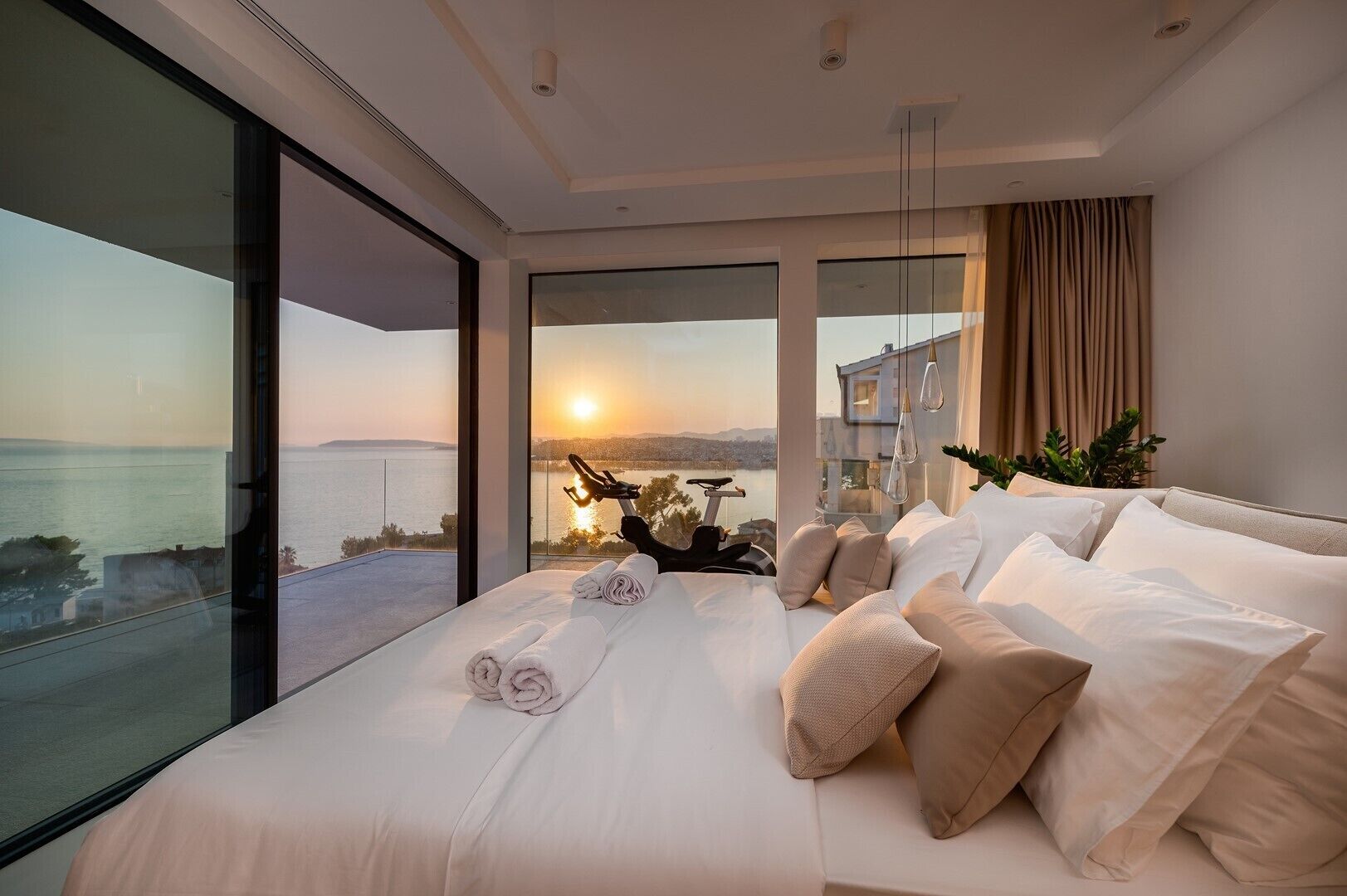A modern bedroom with a large bed, a view of the sea, and a cityscape in the background.