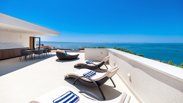 Una terraza moderna al aire libre con vista al mar, amueblada con sillones de descanso y una zona de comedor.