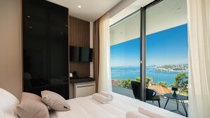 Habitación de hotel con una cama grande, televisión de pantalla plana, escritorio con silla y balcón con vista al mar.