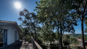 A wooden deck leading to a white building with a sloped roof, surrounded by trees and a hilly landscape.