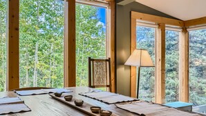 A wooden dining table with placemats and bowls, set against a backdrop of large windows with a forest view. - High Altitude Haven 3 Bedroom Home by RedAwning (Alma)