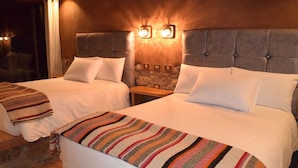 Une chambre d’hôtel avec deux lits, une tête de lit en bois et une table de chevet dotée de deux lampes fixées au mur.