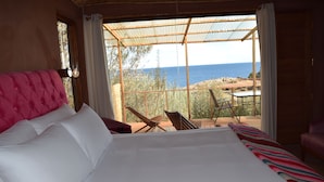 Une chambre avec un grand lit, une vue sur la mer et un balcon équipé de chaises et d’une table.