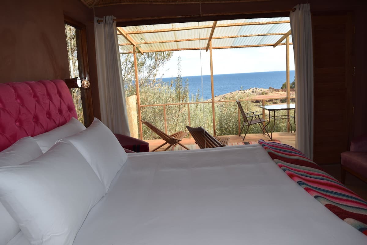 A bedroom with a large bed, a view of the sea, and a balcony with chairs and a table.