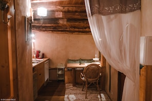 Ein gemütliches Zimmer mit Holzbalkendecke, einem kleinen Tisch mit Stuhl, einem Schreibtisch und einem Bett mit weißem Vorhang.