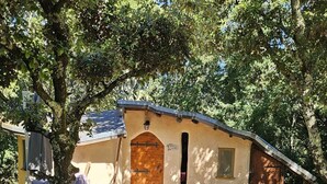 Un bâtiment rustique en bois, doté d’un toit en pente, d’une porte en bois et d’un petit espace porche aménagé avec des sièges.