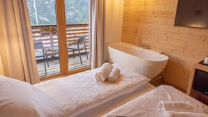 Un dormitorio con dos camas, un muro de madera, una bañera y vistas a un balcón con mobiliario exterior.