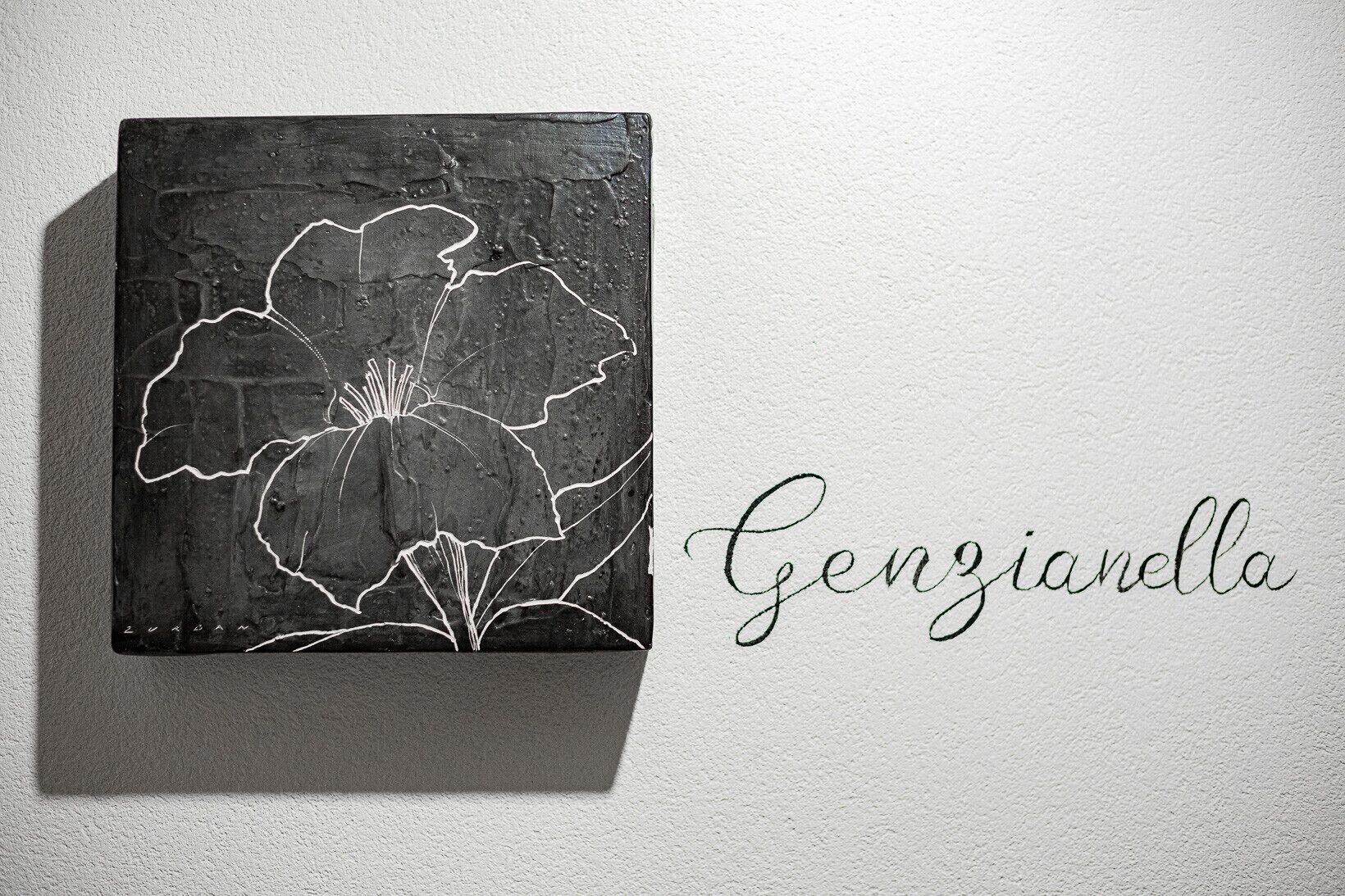 Eine Schwarzweiß-Grafik mit floralem Design und dem Schriftzug 'Genzianella' in Kursivschrift.
