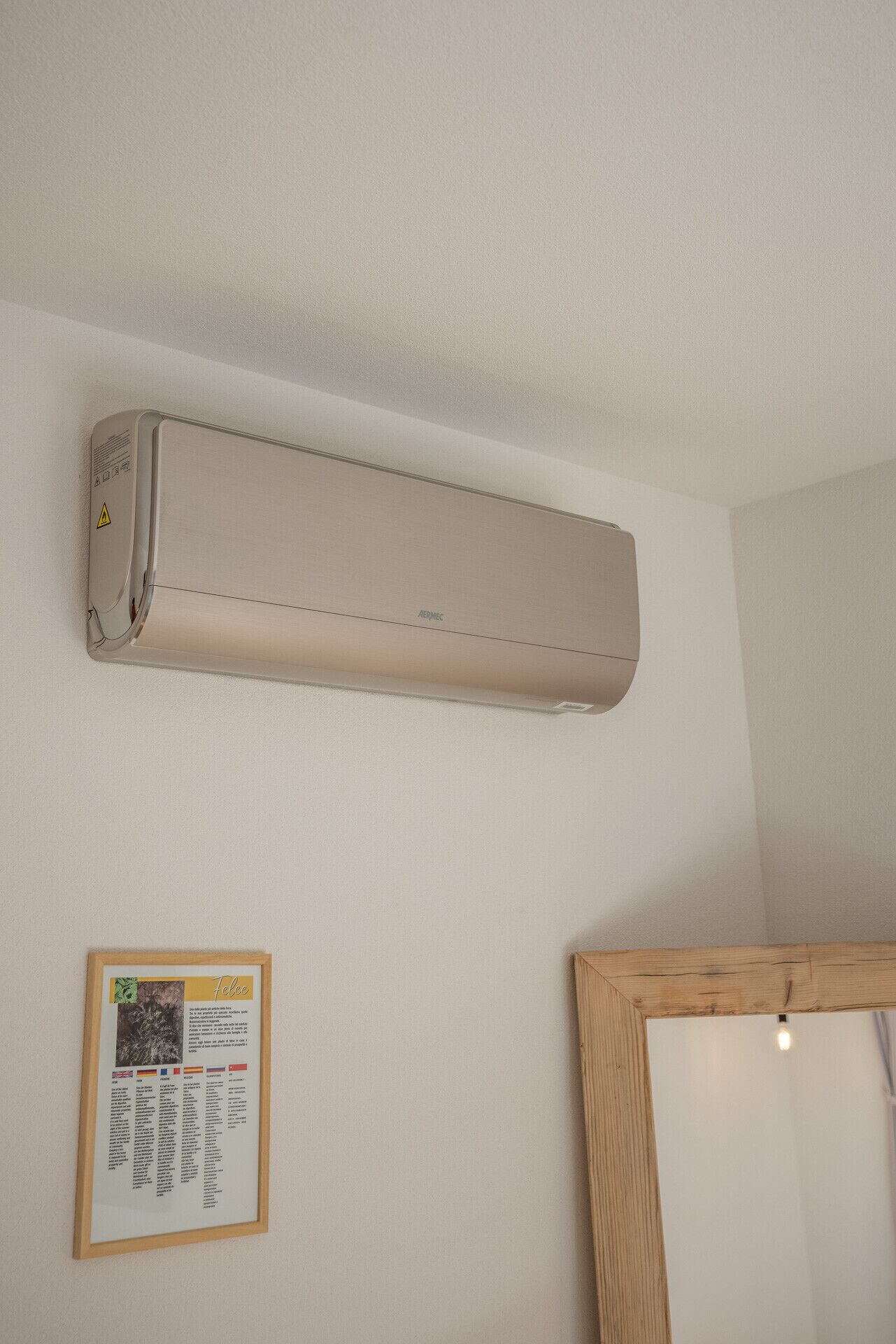 A wall-mounted air conditioner, a framed informational plaque, and a wooden-framed mirror.