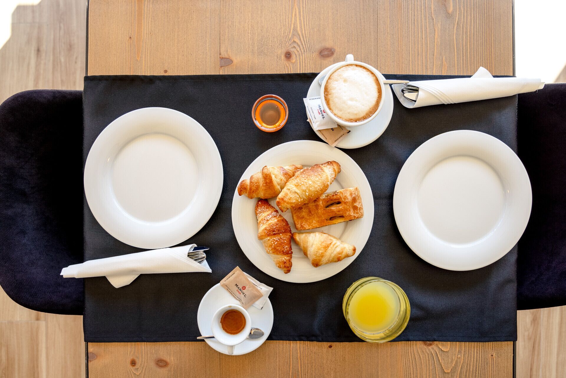 Colazione con croissant, caffè e un bicchiere di succo su un tavolo di legno.