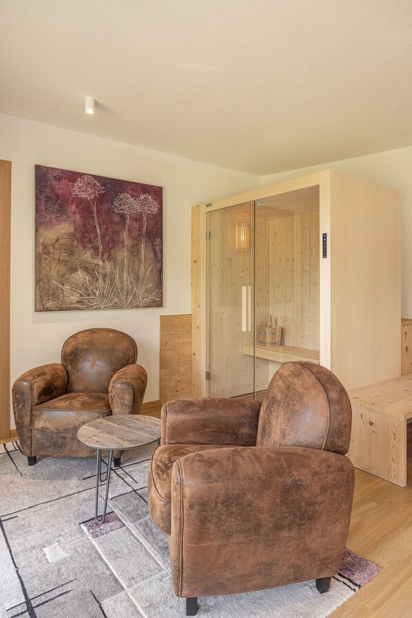 A modern living room with a brown leather sofa, a small round coffee table, and a large abstract painting on the wall.