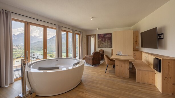 Une salle de spa moderne dotée d’un grand jacuzzi, de meubles en bois et offrant une vue sur les montagnes grâce à de larges fenêtres.