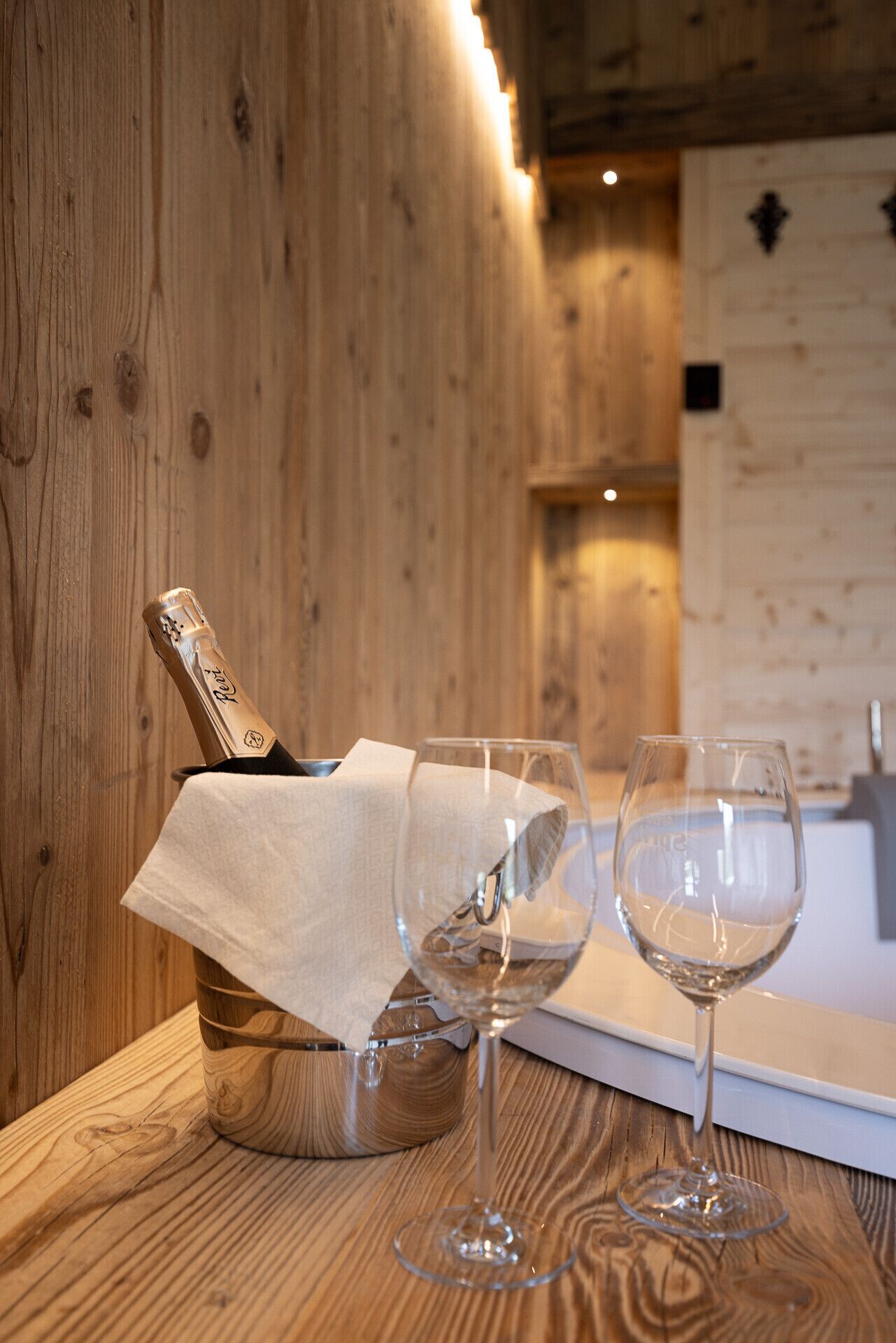 Een houten tafel met een champagnekoeler en twee wijnglazen.