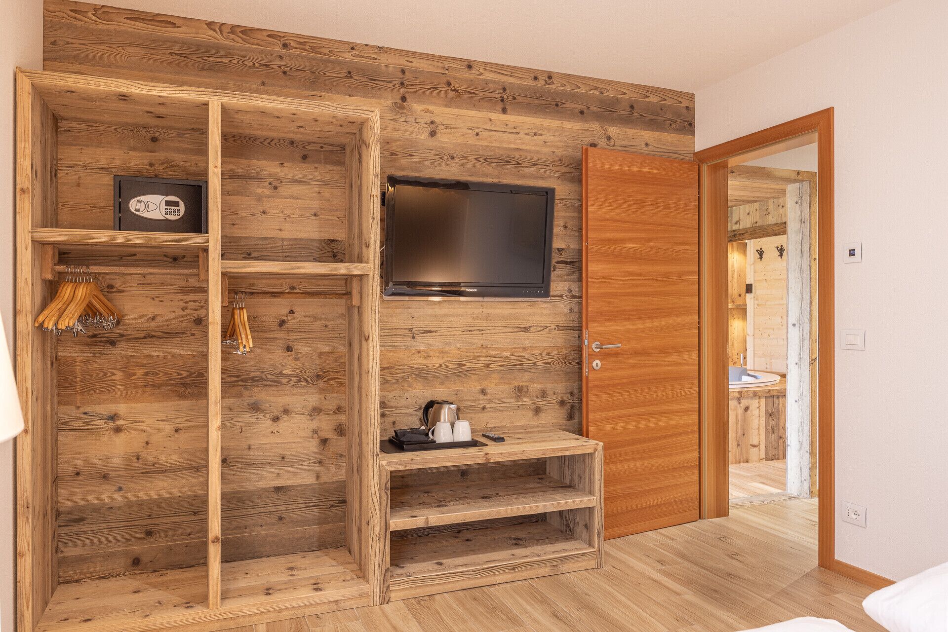 Un intérieur en bois avec un téléviseur fixé au mur, une porte en bois et une étagère sur laquelle se trouvent une bouilloire et des tasses.
