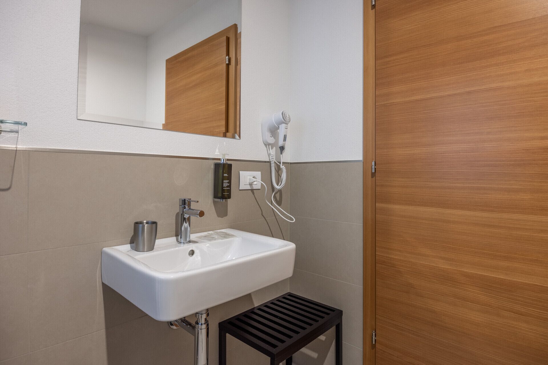A bathroom with a white sink, a mirror, a hairdryer, and a wooden door.