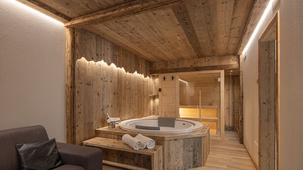 Ein Holzinnenraum mit einer Badewanne, einer Bank mit Handtüchern und einem Sofa.