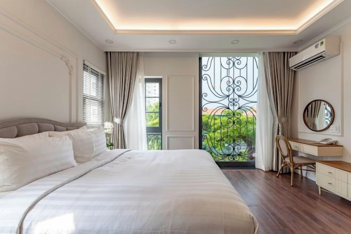 Un dormitorio moderno con una cama grande, un escritorio y vistas a la vegetación a través de una ventana.