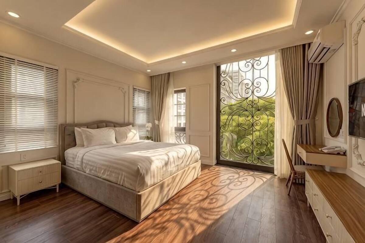 Ein Schlafzimmer mit einem großen Bett, einem Nachttisch, einer Kommode, einem Fernseher und einem Fenster mit Vorhängen.